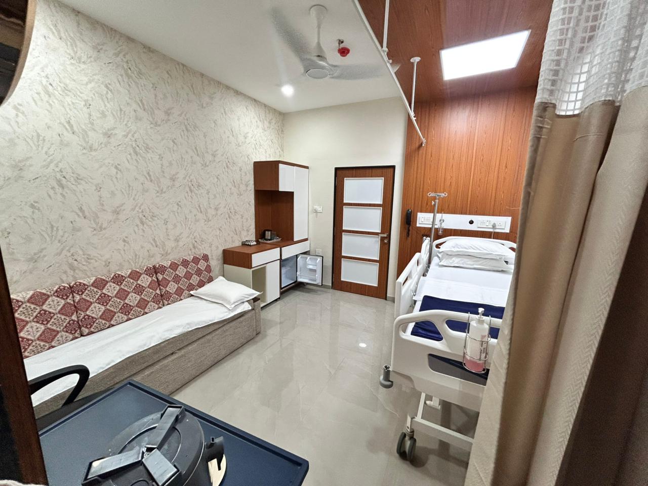 Room overview — adjustable bed, attendant bench and over-bed patient table.